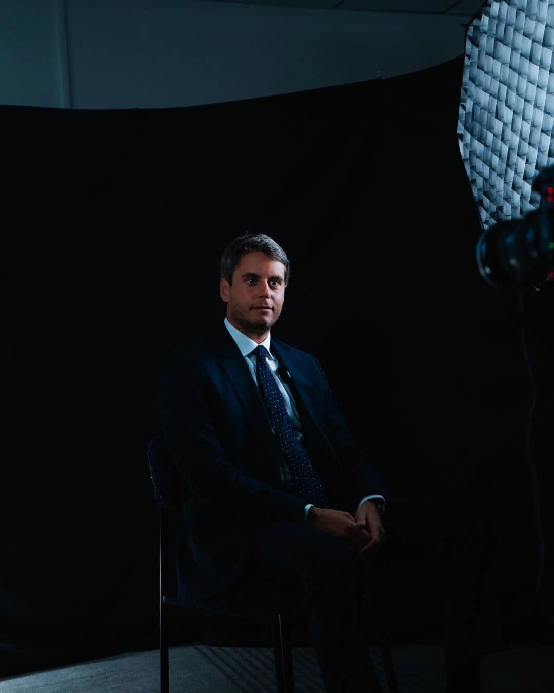 Gabriel Attal sur un fond noir avec un projecteur lançant un regard rassurant