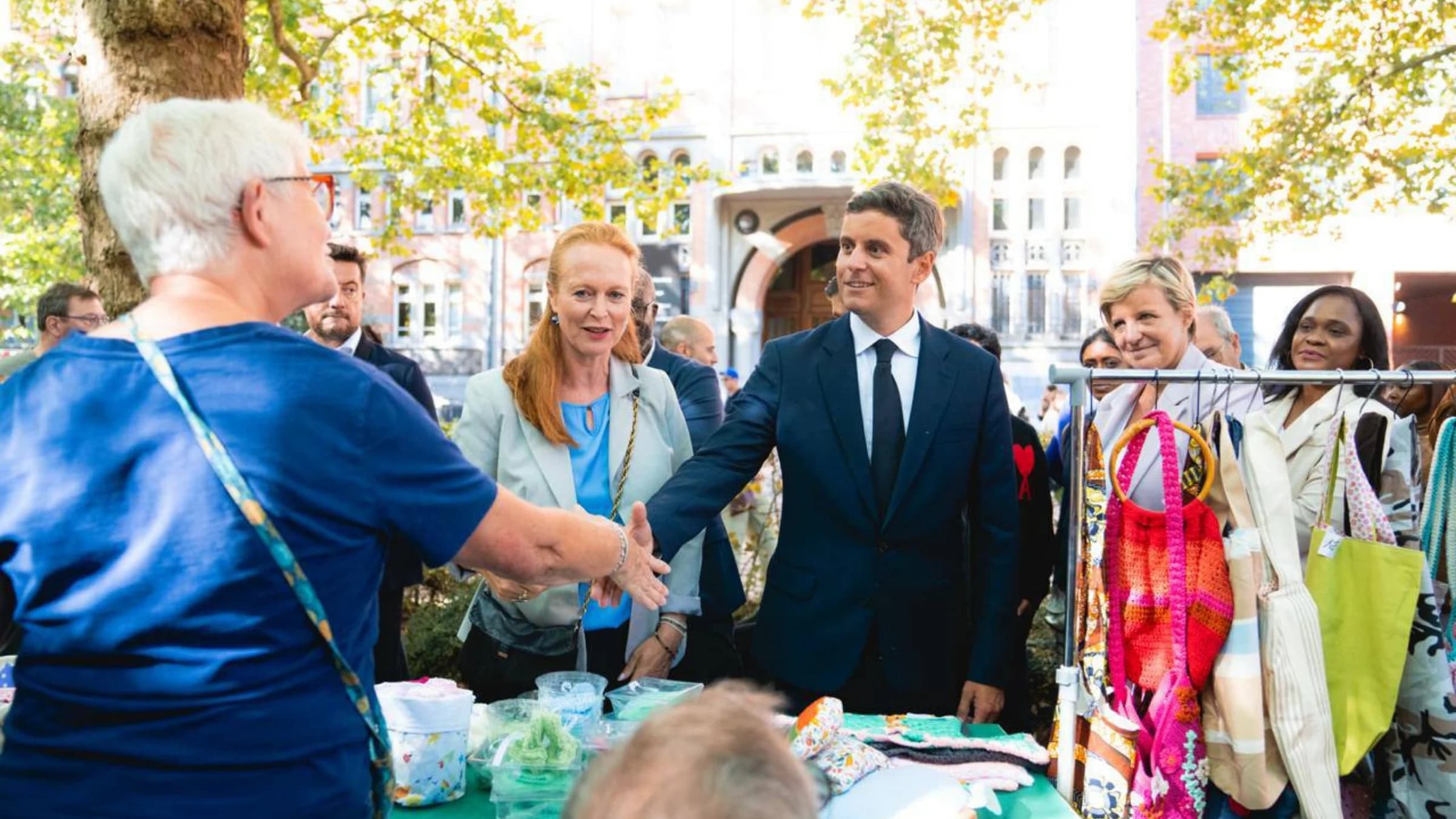 Gabriel Attal en train de serrer la main à un home tenant un stand. A ses côtés Violette Spillebout 