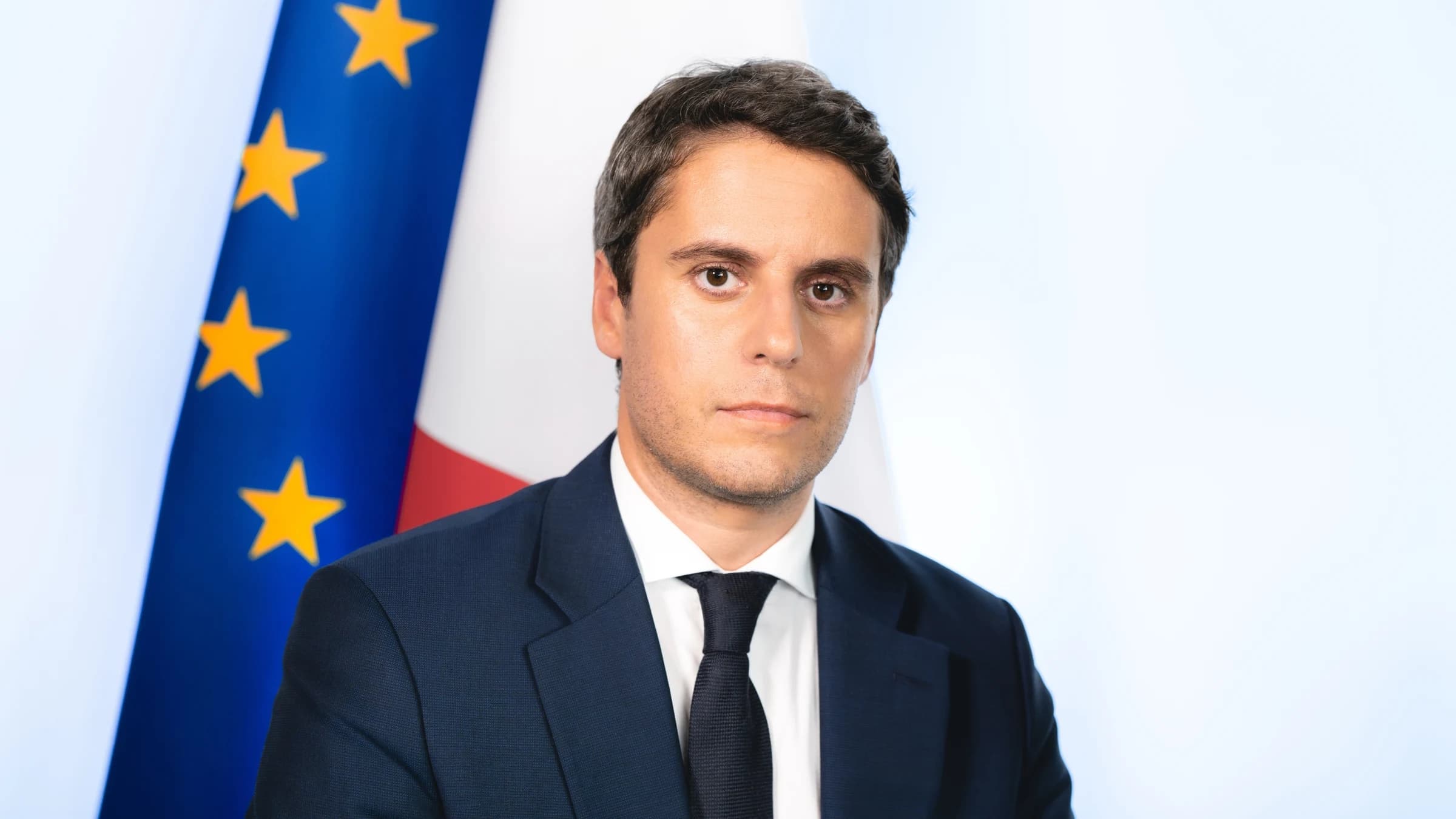 Gabriel Attal confiant avec des drapeaux européens et français en fond. 