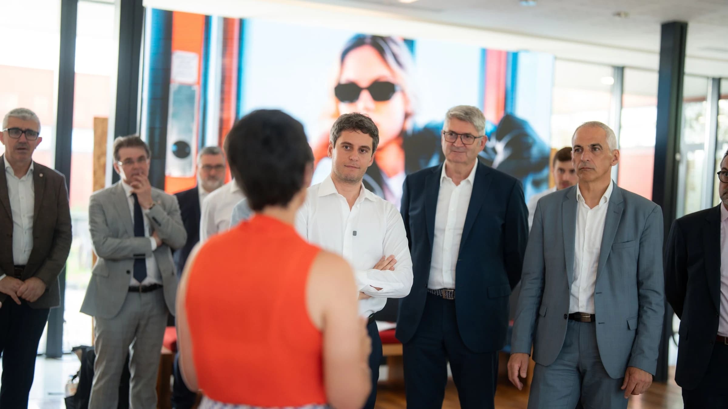 Gabriel Attal en chemise blanche les bras croisées écoutant une dame avec un haut rouge. 