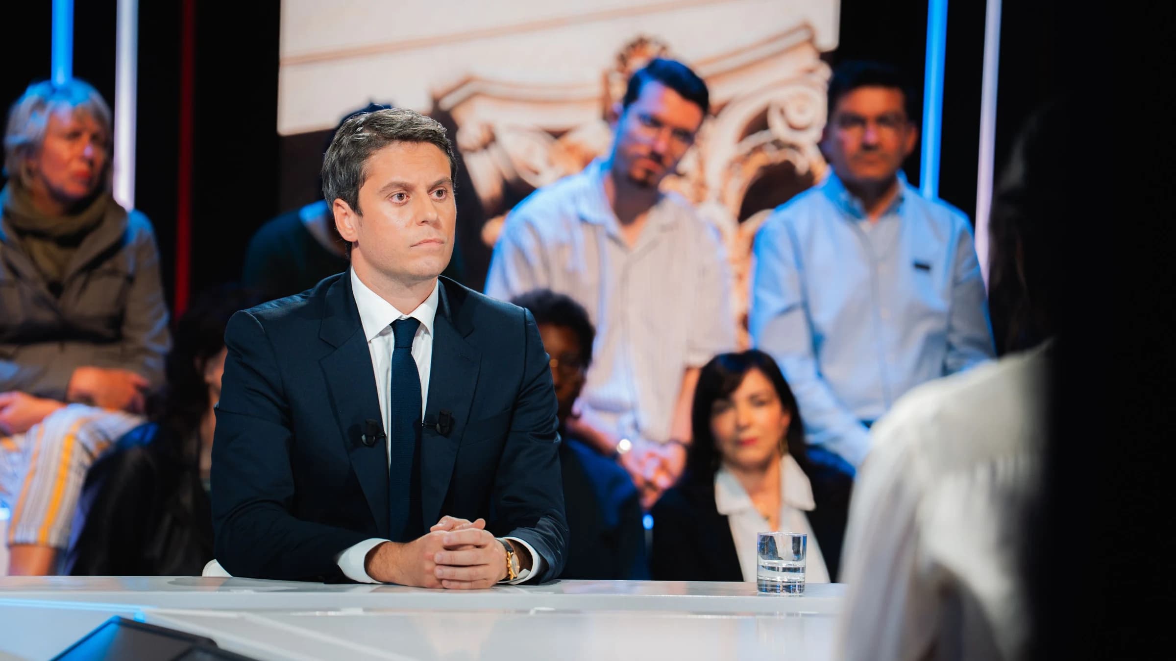 Gabriel Attal, en costume sombre et cravate, assis sur le plateau de BFMTV face au public, lors d’une émission politique.