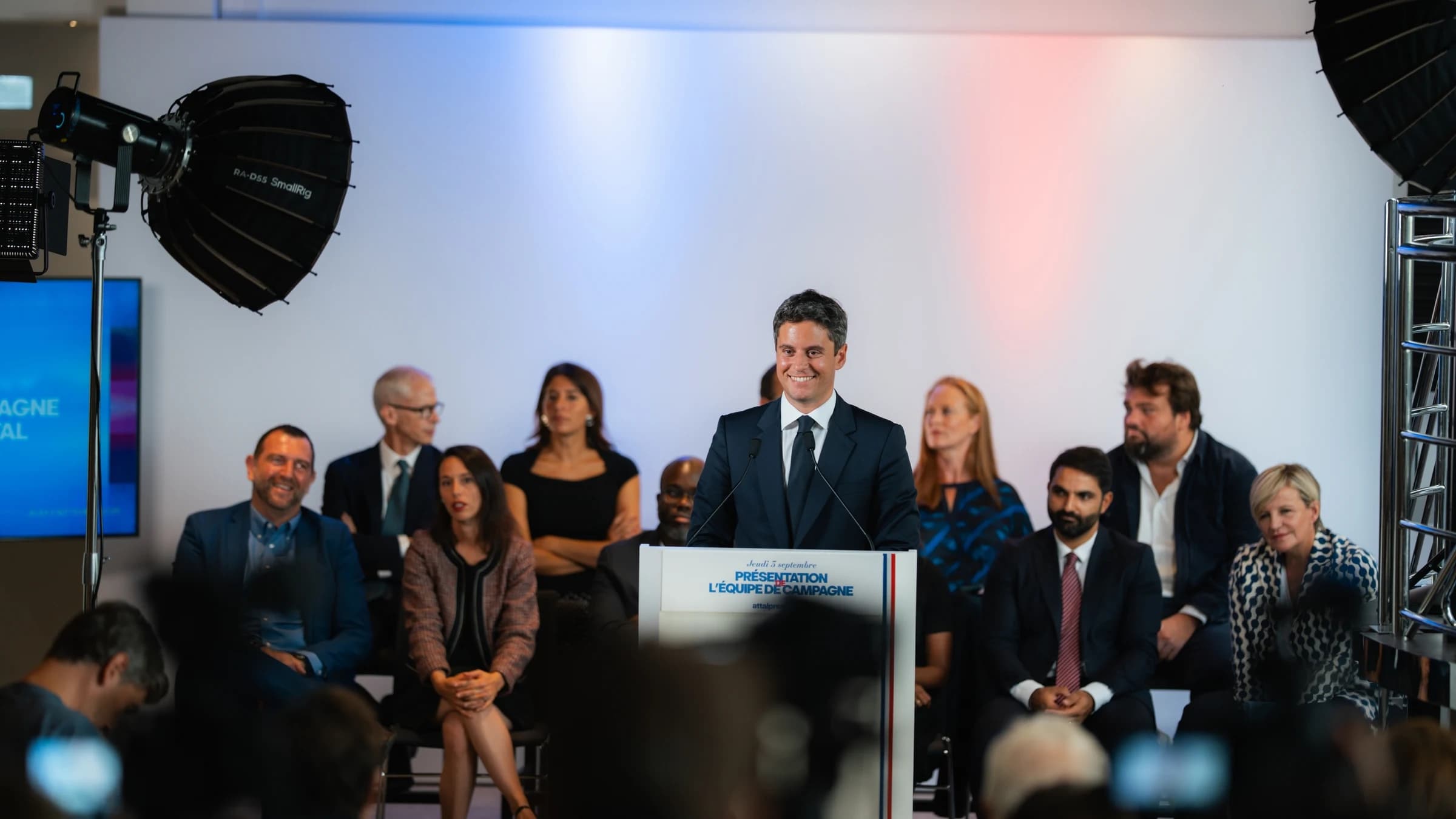 Gabriel Attal assez souriant s'exprime sur son pupitre avec en fond l'ensemble de son équipe qui l'écoute 