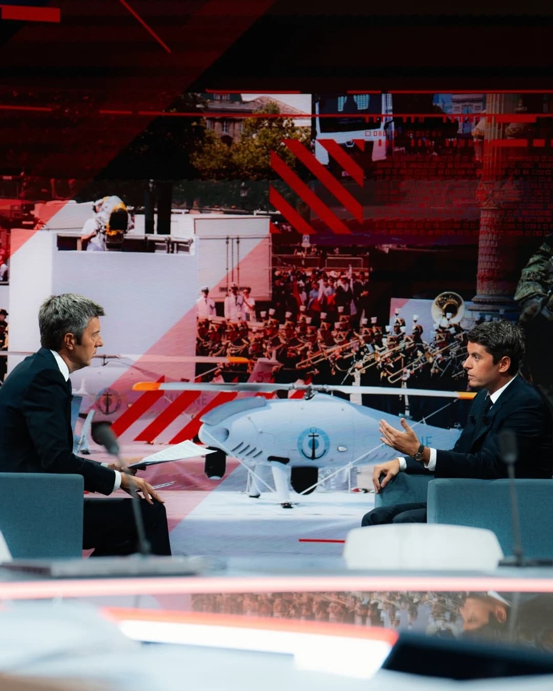 Gabriel Attal sur le plateau de BFM en train d'échanger avec un journaliste. Tout deux assis avec un air assez sérieux. 