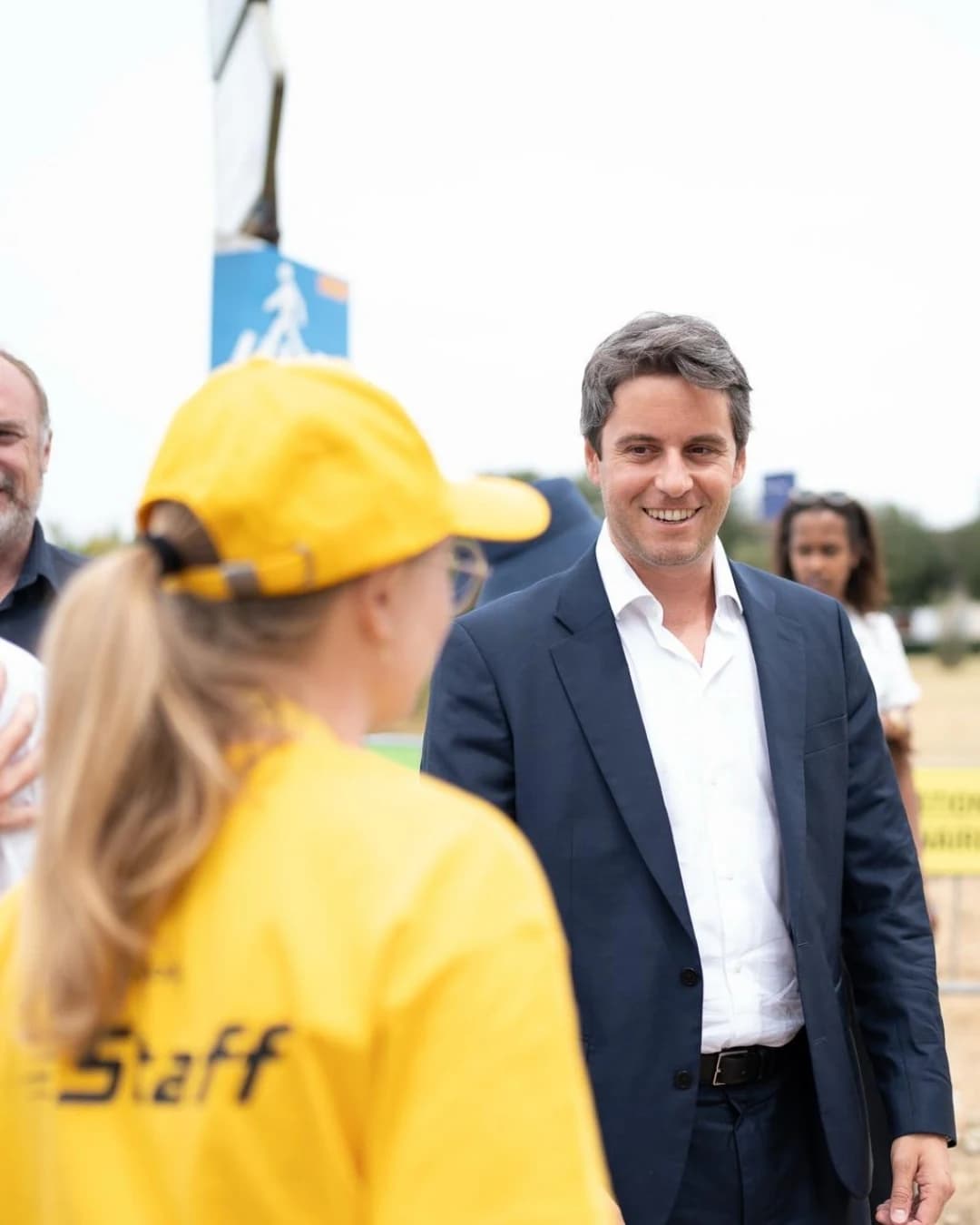 Gabriel Attal souriant à une femme avec la tenue jaune du Tour de France