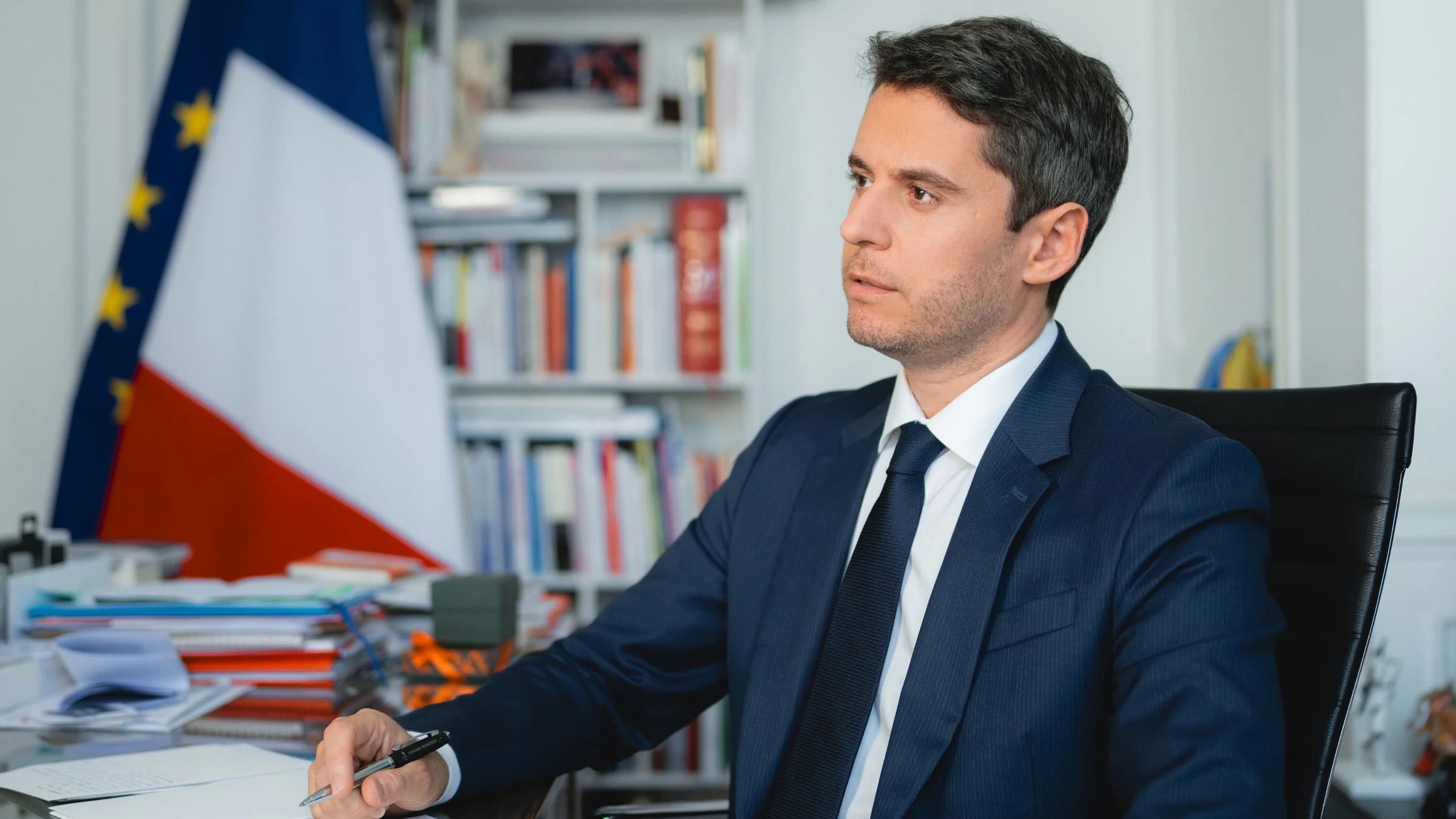 Gabriel Attal en train de réfléchir avec un drapeau français en fond
